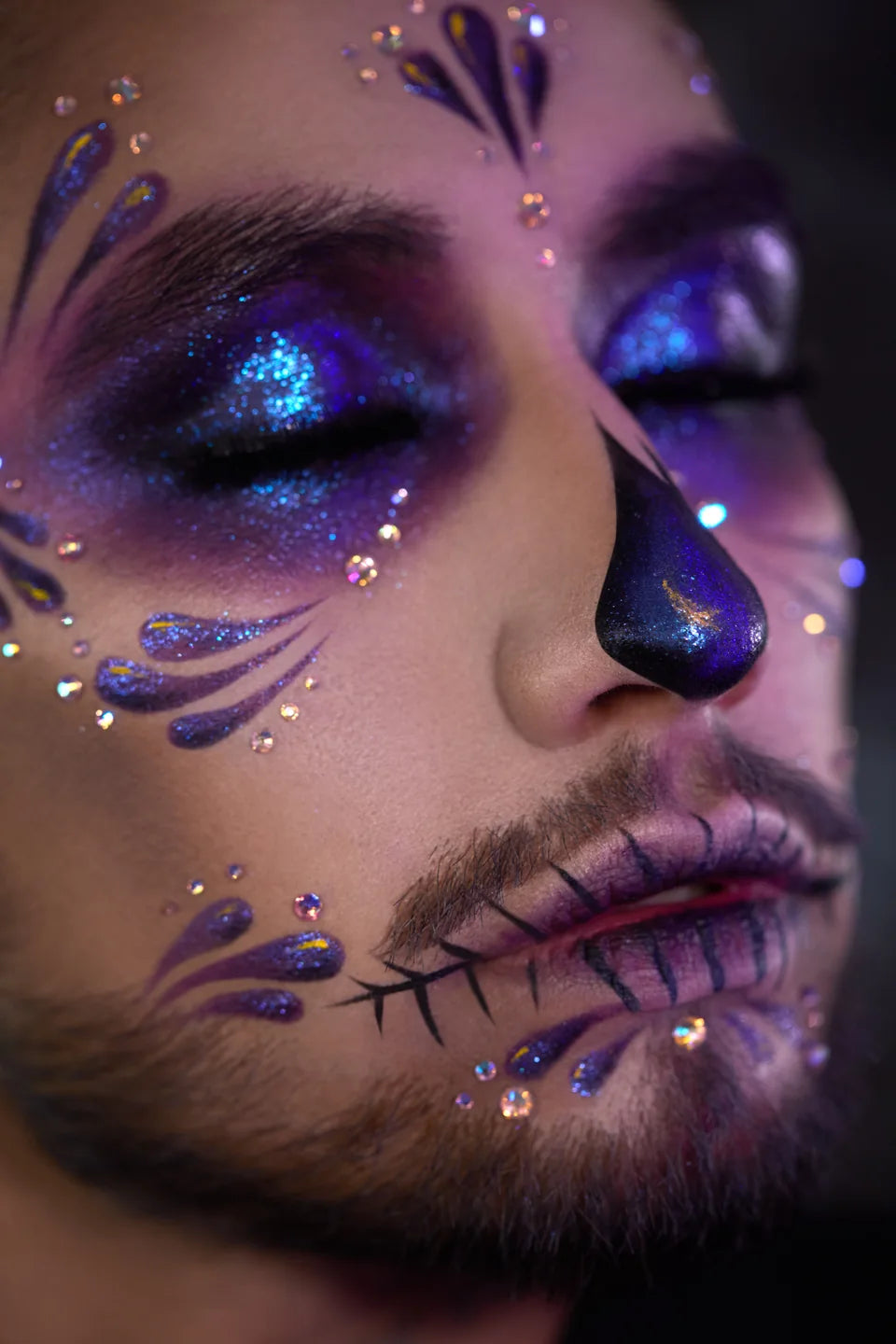 Purple and electric-blue shimmer skull makeup with rhinestone details