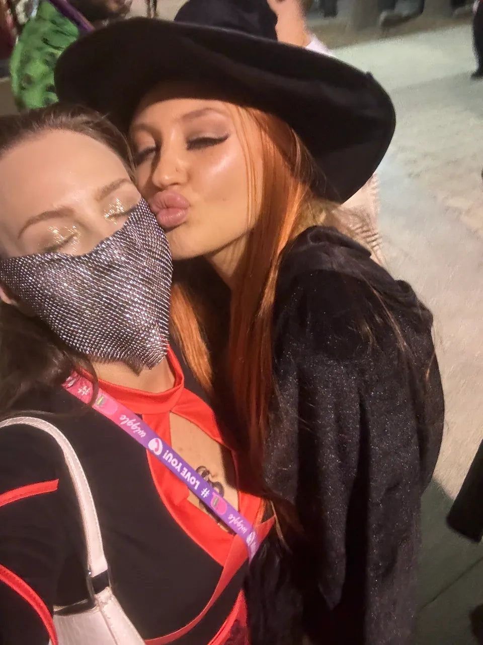 Two friends at a festival wearing sparkling eye makeup, a jeweled mask and a black cowboy hat
