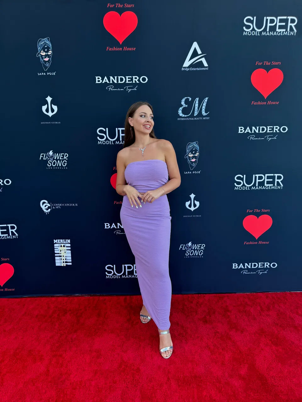 Woman in a lavender dress on a red carpet in front of an event backdrop