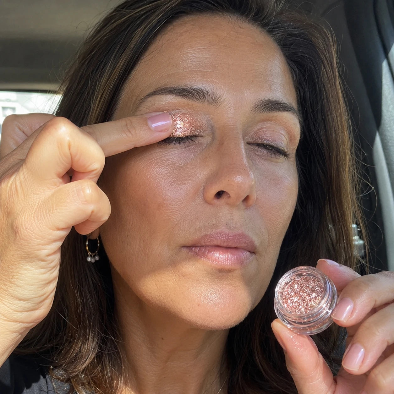 A mature brunette woman applying pink shimmer with her fingertip