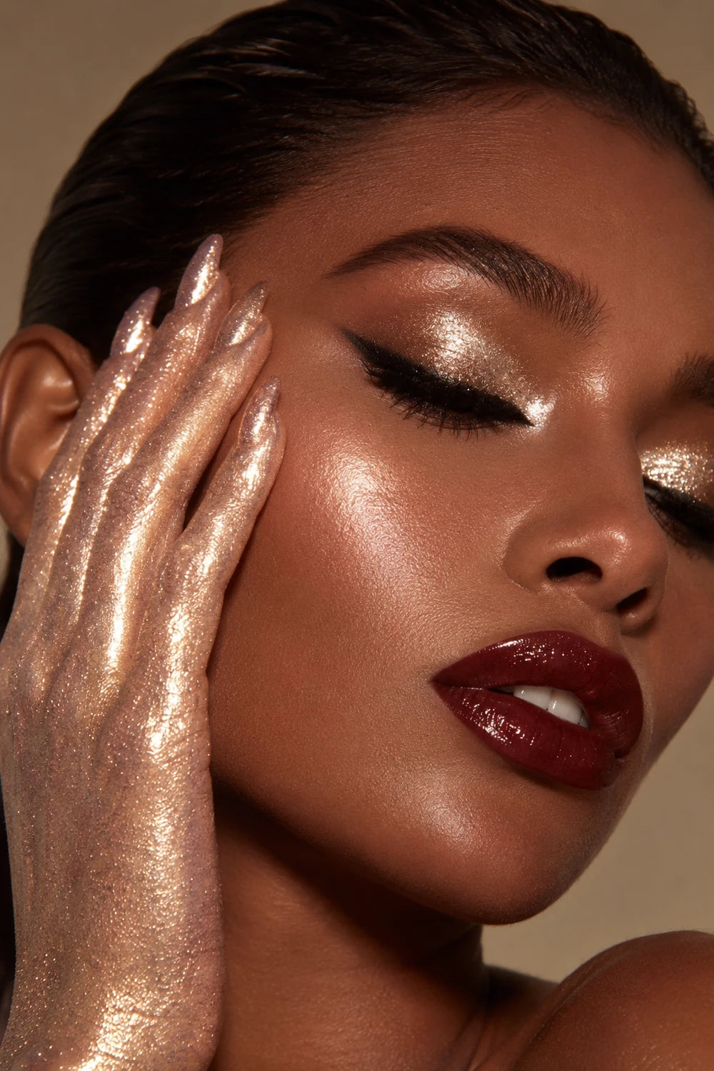 Close-up beauty portrait with champagne shimmer on the eyelids, cheek and hand, and deep burgundy lips