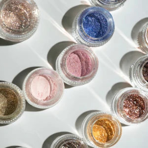 Open pigment jars in blue, pink, gold and bronze tones arranged in sunlight